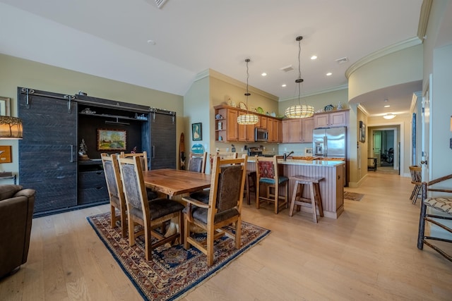 dining area featuring light wood-style floors, visible vents, crown molding, and a barn door