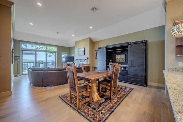 dining room with light wood-style floors, baseboards, visible vents, and a stone fireplace