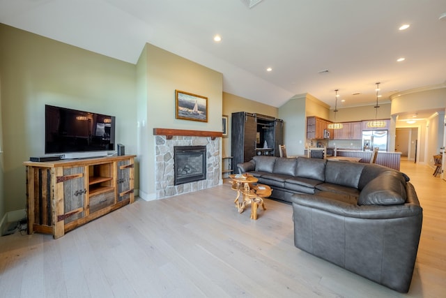 living area featuring recessed lighting, vaulted ceiling, a stone fireplace, light wood-type flooring, and baseboards