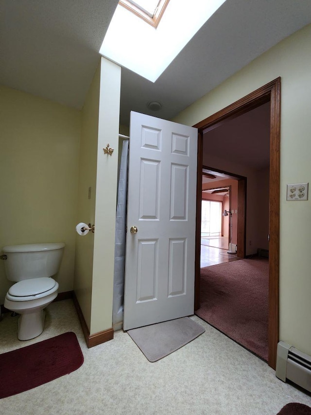 bathroom with a skylight, toilet, and a baseboard heating unit