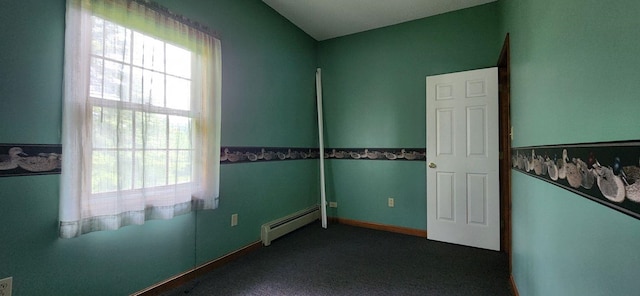 empty room featuring baseboard heating and dark colored carpet