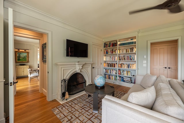 living area featuring light wood finished floors, a fireplace with flush hearth, ornamental molding, and a ceiling fan