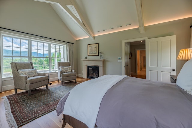 bedroom featuring high vaulted ceiling, baseboards, wood finished floors, beam ceiling, and a glass covered fireplace