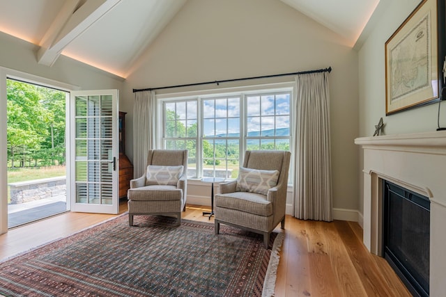 sitting room featuring high vaulted ceiling, baseboards, wood finished floors, beam ceiling, and a glass covered fireplace