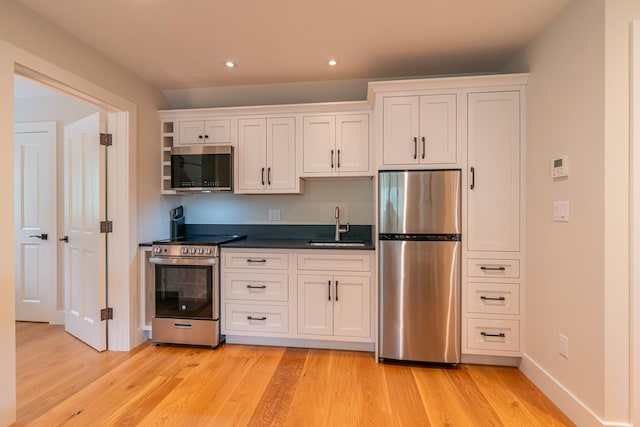 kitchen with dark countertops, a sink, stainless steel appliances, and light wood-style floors