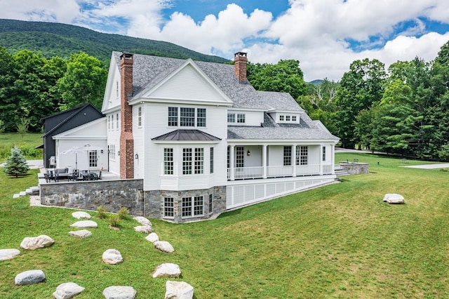 back of property with a chimney, a patio, a shingled roof, and a lawn