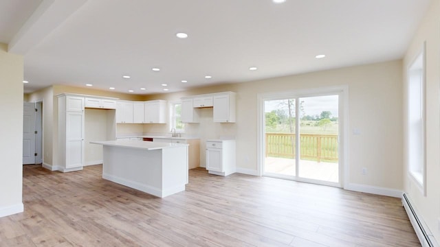 kitchen featuring white cabinets, a baseboard heating unit, a center island, and light hardwood / wood-style flooring