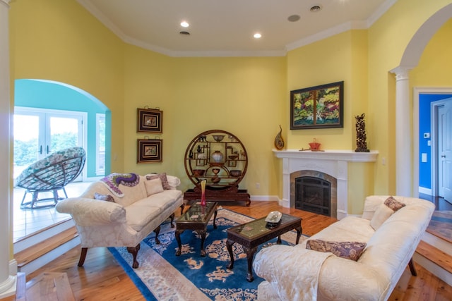 living room with ornate columns, ornamental molding, a tile fireplace, light hardwood / wood-style floors, and a high ceiling