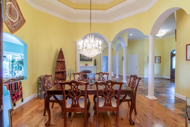 dining room featuring ornate columns, ornamental molding, a towering ceiling, and light hardwood / wood-style floors