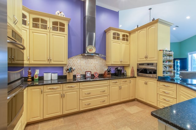 kitchen featuring light brown cabinetry, oven, dark stone counters, black electric stovetop, and wall chimney range hood