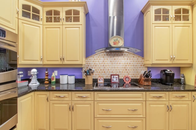 kitchen with light brown cabinetry, backsplash, dark stone counters, wall chimney range hood, and black electric cooktop