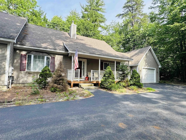 view of front of property featuring a shingled roof, a detached garage, a chimney, and a porch