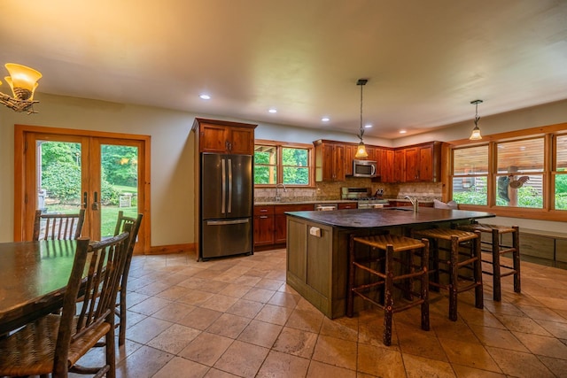 kitchen featuring decorative backsplash, dark countertops, appliances with stainless steel finishes, hanging light fixtures, and french doors