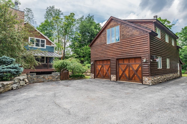 view of home's exterior with stone siding, faux log siding, driveway, and a garage