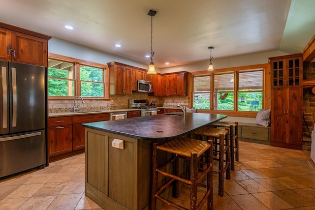 kitchen featuring decorative light fixtures, stainless steel appliances, backsplash, a kitchen island, and a sink