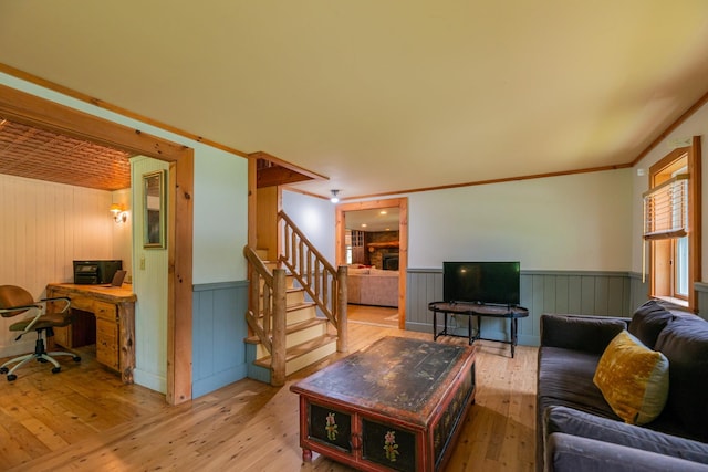 living area with stairs, ornamental molding, a wainscoted wall, and light wood-style flooring