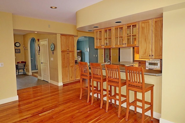 kitchen with hardwood / wood-style flooring, fridge, a kitchen breakfast bar, and oven