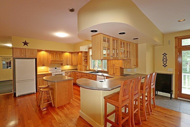 kitchen with sink, white appliances, light hardwood / wood-style flooring, a breakfast bar area, and kitchen peninsula