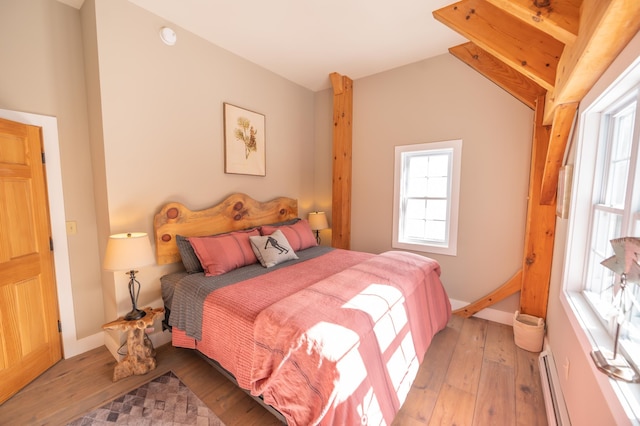 bedroom with multiple windows, lofted ceiling, a baseboard heating unit, and light hardwood / wood-style flooring