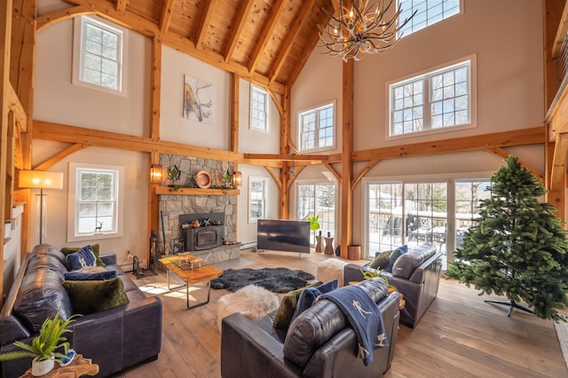 living room with light hardwood / wood-style flooring, beam ceiling, a towering ceiling, a notable chandelier, and a wood stove