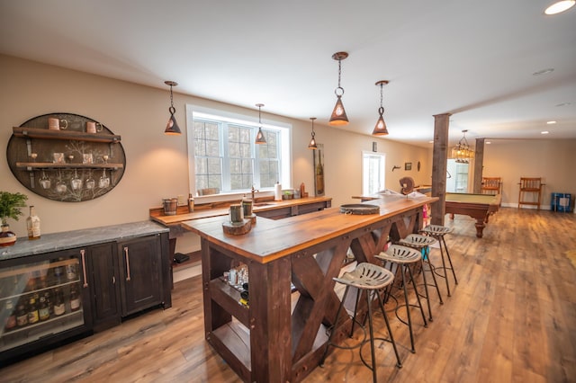 bar with dark brown cabinetry, sink, pendant lighting, beverage cooler, and light hardwood / wood-style floors