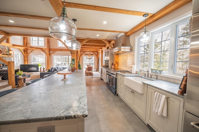 kitchen with a spacious island, wall chimney exhaust hood, sink, pendant lighting, and stainless steel appliances