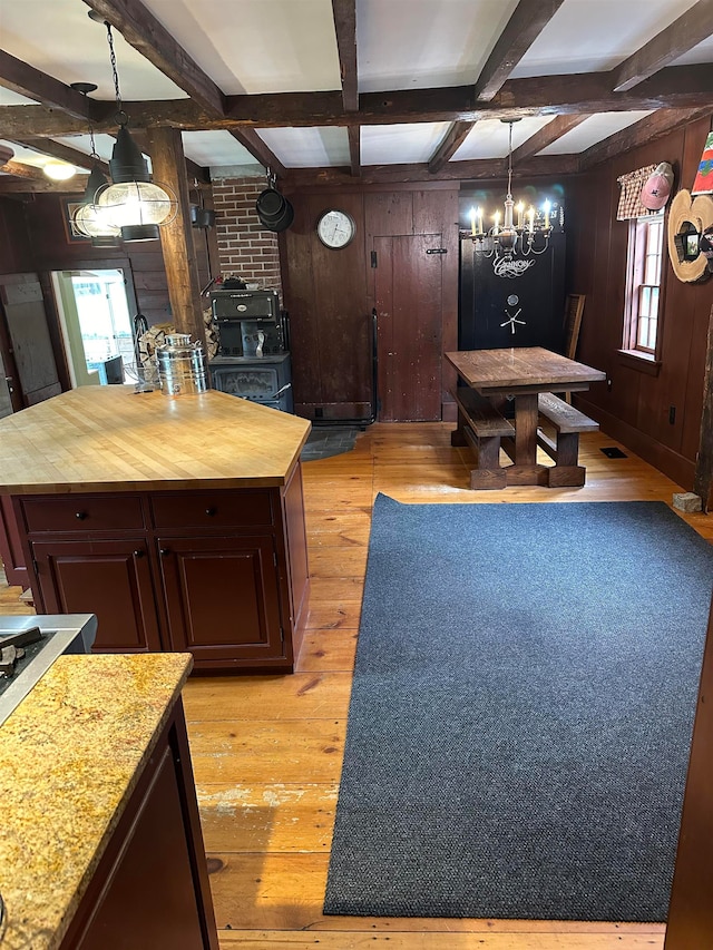 kitchen with hanging light fixtures, beamed ceiling, wood walls, and light hardwood / wood-style flooring