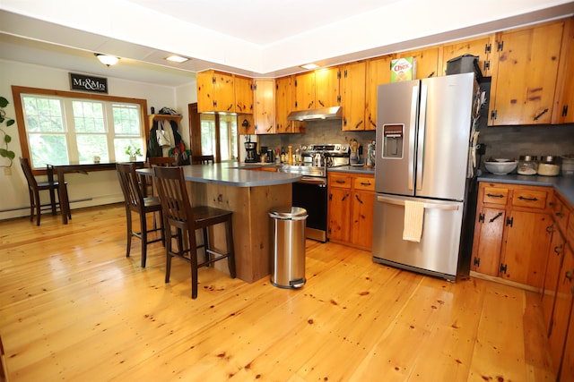 kitchen featuring appliances with stainless steel finishes, light wood-type flooring, a kitchen bar, and decorative backsplash