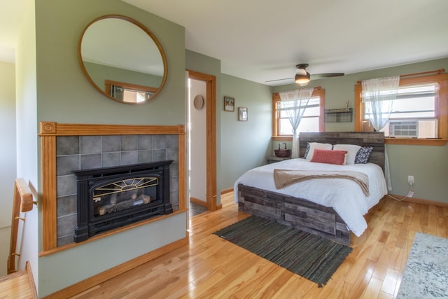 bedroom with a tile fireplace, light wood-type flooring, and ceiling fan