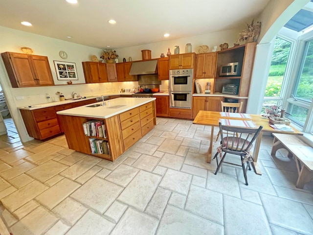 kitchen featuring sink, stainless steel appliances, range hood, decorative backsplash, and a center island with sink