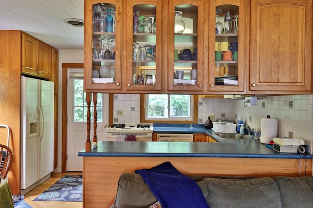 kitchen featuring sink, white appliances, a breakfast bar, backsplash, and kitchen peninsula