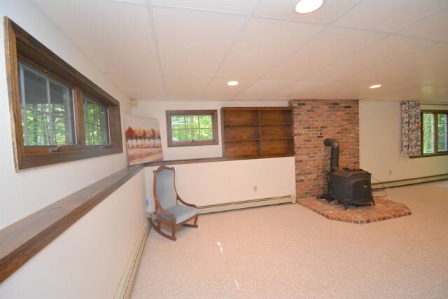 sitting room featuring a baseboard heating unit, a wood stove, and a wealth of natural light