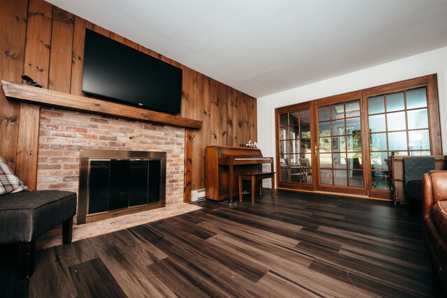 living room featuring a brick fireplace, wood walls, baseboard heating, and dark hardwood / wood-style flooring