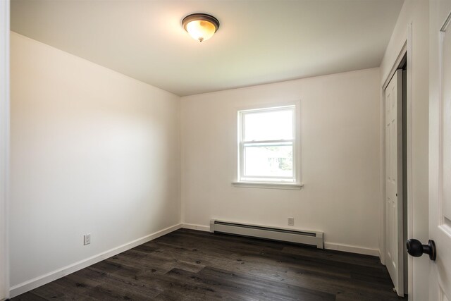 unfurnished bedroom featuring baseboards, a closet, a baseboard heating unit, and dark wood-style flooring