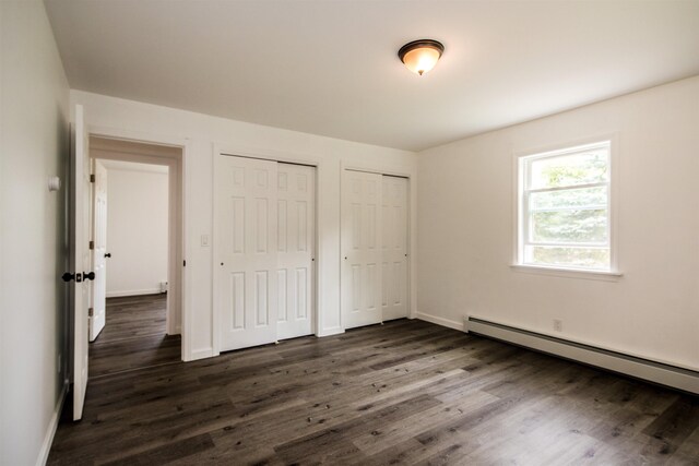 unfurnished bedroom with dark wood-style floors, a baseboard radiator, baseboards, and multiple closets