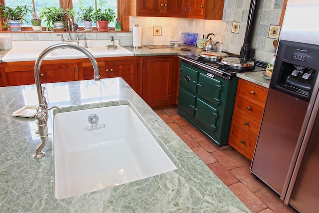 kitchen featuring tasteful backsplash, sink, light stone countertops, and stainless steel refrigerator with ice dispenser