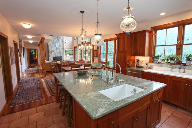 kitchen with a breakfast bar, decorative light fixtures, an island with sink, sink, and light stone countertops