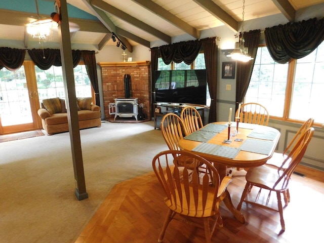 dining area featuring vaulted ceiling with beams, carpet, a healthy amount of sunlight, and a wood stove