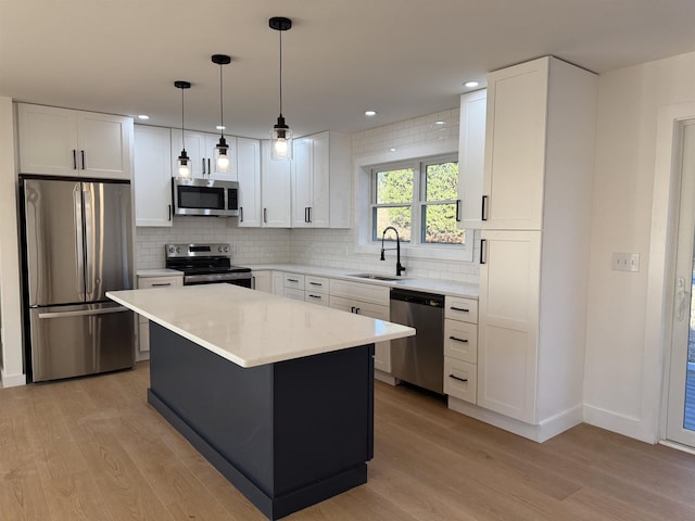 kitchen with a sink, white cabinets, light wood-style floors, appliances with stainless steel finishes, and tasteful backsplash