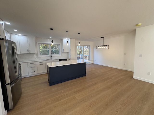 kitchen with a sink, light countertops, backsplash, freestanding refrigerator, and a center island