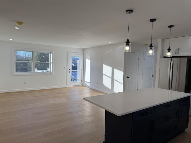 kitchen featuring baseboards, freestanding refrigerator, dark cabinetry, light wood-style floors, and pendant lighting