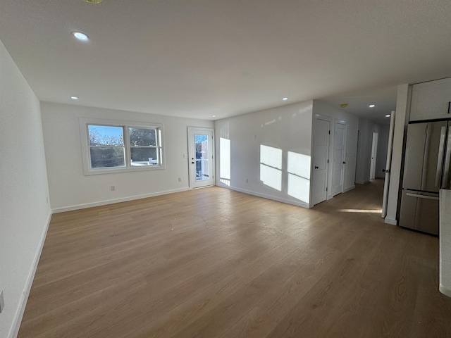 unfurnished living room with recessed lighting, light wood-type flooring, and baseboards