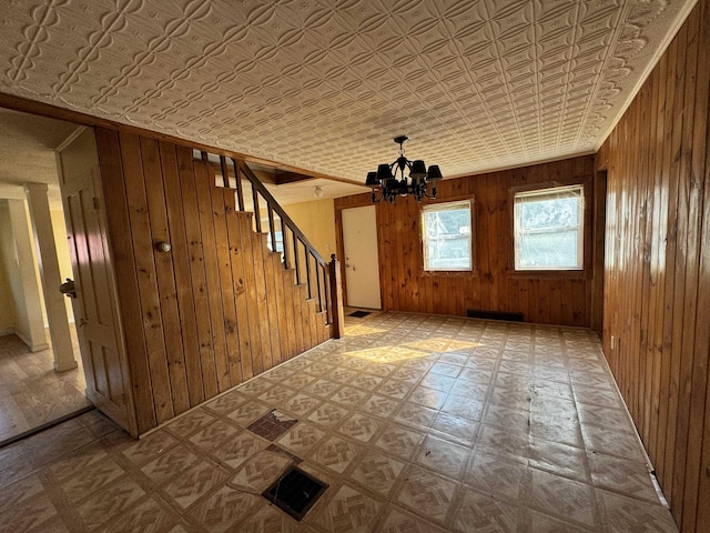 empty room featuring tile patterned floors, an ornate ceiling, wood walls, a chandelier, and stairs