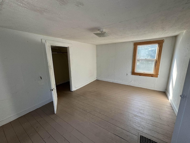 spare room with visible vents, baseboards, a textured ceiling, and hardwood / wood-style floors