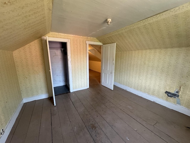 additional living space with baseboards, lofted ceiling, dark wood finished floors, and wallpapered walls