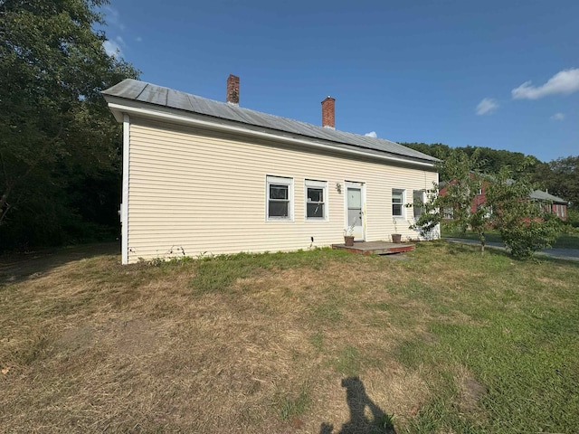 back of house featuring roof mounted solar panels, a chimney, and a yard