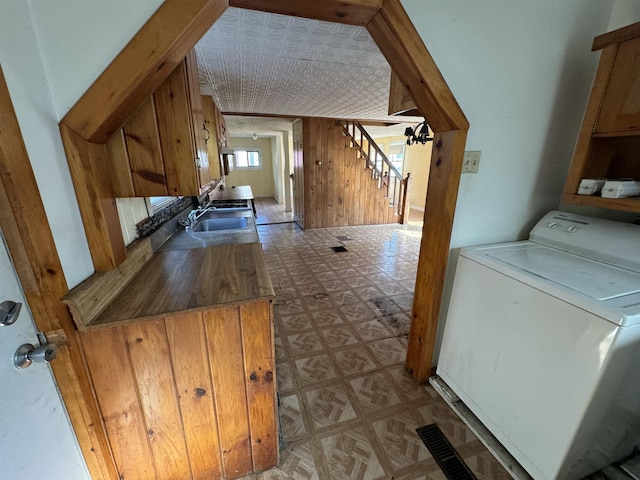 clothes washing area featuring tile patterned floors, a sink, washer / clothes dryer, wooden walls, and laundry area