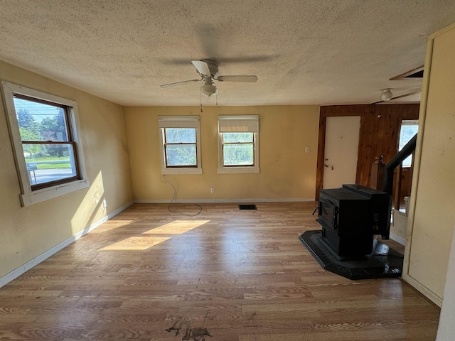 unfurnished living room with a ceiling fan, wood finished floors, baseboards, a wood stove, and a textured ceiling