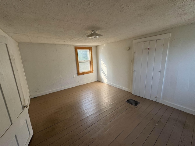 unfurnished bedroom with hardwood / wood-style flooring, baseboards, visible vents, and a textured ceiling