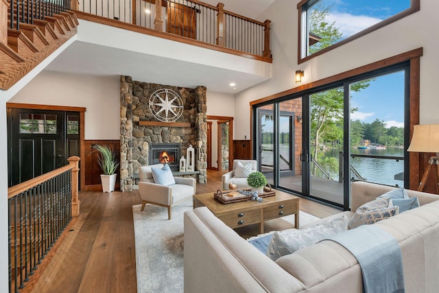 living room featuring a stone fireplace, wood walls, wood-type flooring, a high ceiling, and a water view